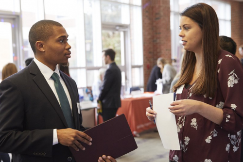 Young man and young woman in professional clothing speaking to each other in the Dining Commons.