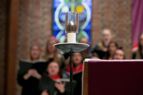 Candle in Chapel of Mary; Choir members are out of focus behind candle.