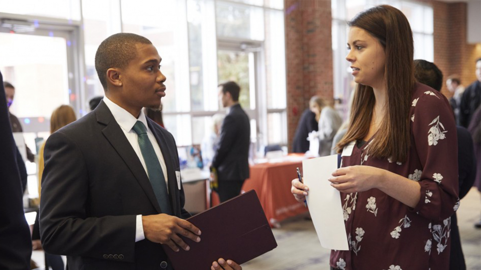 Young man and young woman in professional clothing speaking to each other in the Dining Commons.