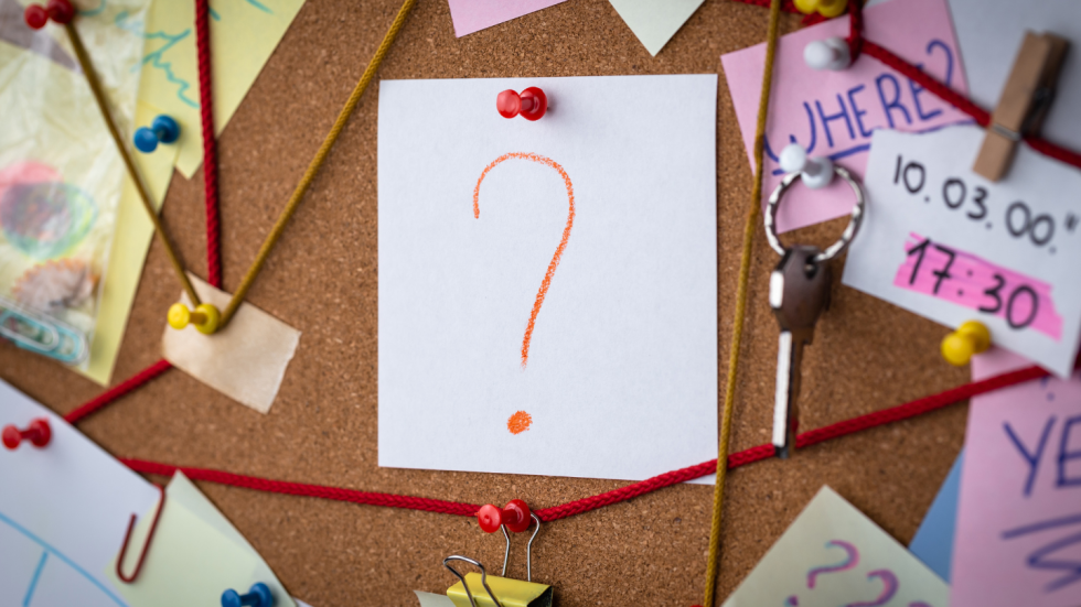 Bulletin board filled with papers; white piece of paper with "?" on it is in the middle of the board.