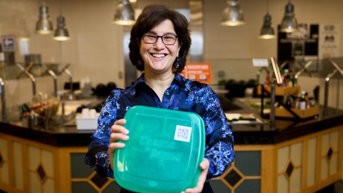 Cheryl Schnitzer in Dining Commons holding green container.