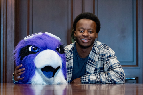 Elijah Byrd '27 sitting at table; Ace the Skyhawk mask is resting on table.