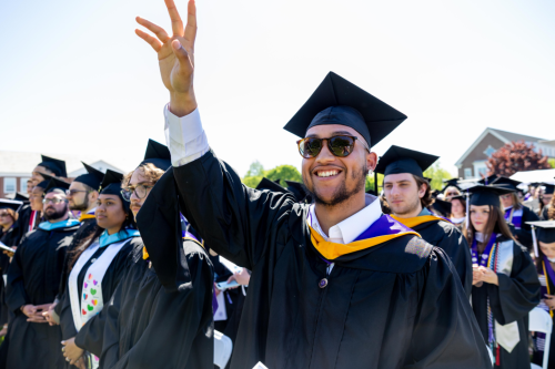 Student raising hand while wearing graduation regalia