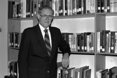James J. Kenneally in front of bookshelf, photograph in black and white