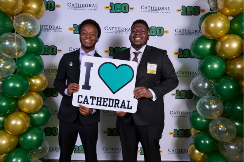 Stonehill students Elijah Byrd '27 (left) and Peterson Charles '27 (right) holding a sign that reads "I Love Cathedral"