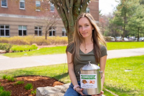 Emma Worster holding a compost bin while sitting on ledge.