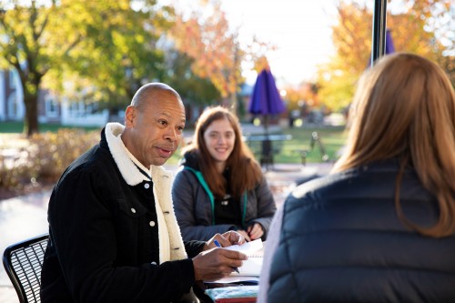 Dr. Myers outside, seated, talking with two female students.
