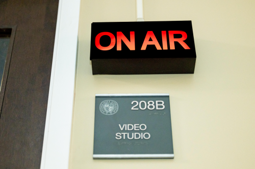 Red "on air" sign is lit up above another sign that reads "208B Video Studio"