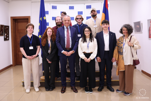 A group of people with name badges stands together in front of European Union and Armenian flags, posing for a photo indoors.