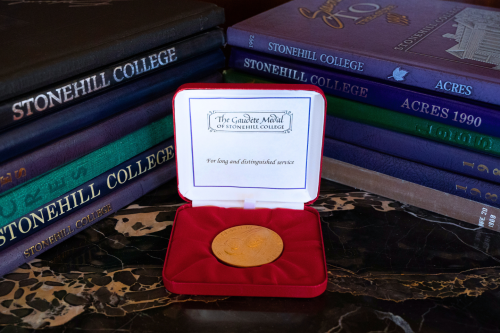 The Gaudete Medal on a table, surrounded by two stacks of Stonehill yearbooks.