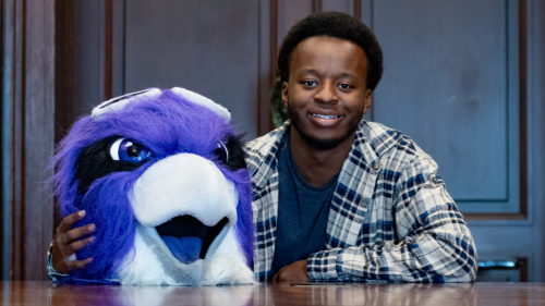 Elijah Byrd '27 sitting at table; Ace the Skyhawk mask is resting on table.