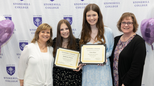 Four people are smiling and standing together, with two of them holding certificates from Stonehill College.