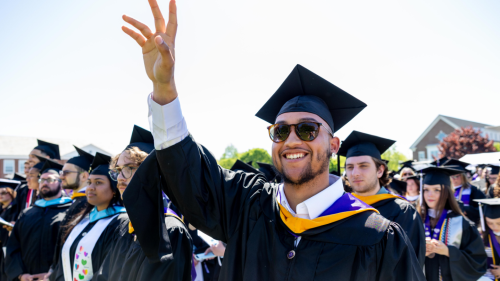 Student raising hand while wearing graduation regalia