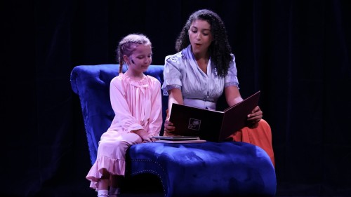 Playing the part of "Nanny," Ariana Barbosa ’27 reads a bedtime story to a child in a scene from "Murder on the Orient Express."