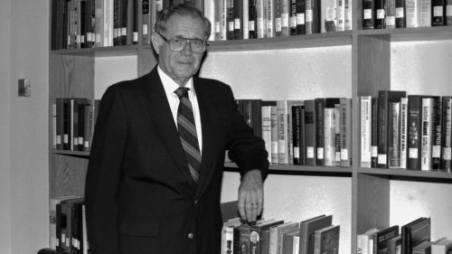 James J. Kenneally in front of bookshelf, photograph in black and white