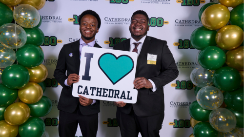Stonehill students Elijah Byrd '27 (left) and Peterson Charles '27 (right) holding a sign that reads "I Love Cathedral"