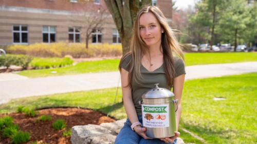 Emma Worster holding a compost bin while sitting on ledge.