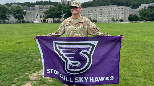 Francisco Melendez ’27 wearing Army uniform, holding Stonehill Skyhawks flag.