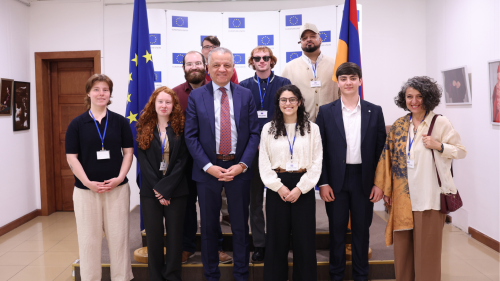 A group of people with name badges stands together in front of European Union and Armenian flags, posing for a photo indoors.