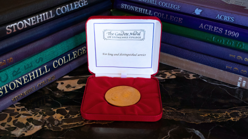 The Gaudete Medal on a table, surrounded by two stacks of Stonehill yearbooks.