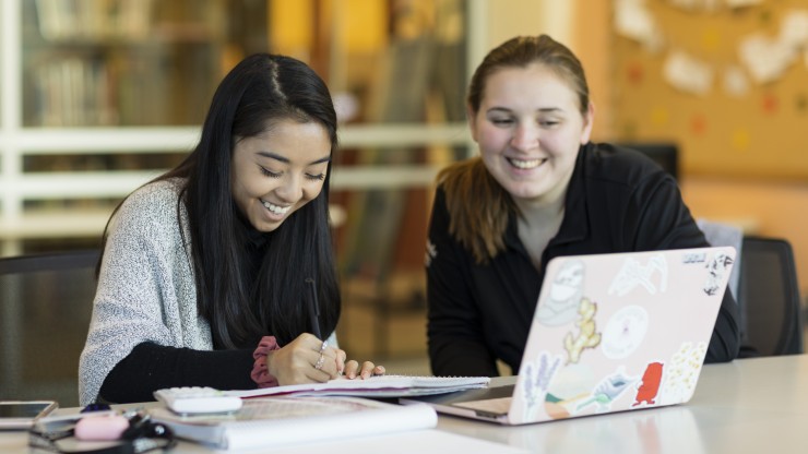 Two female students looking at a laptop and smiling